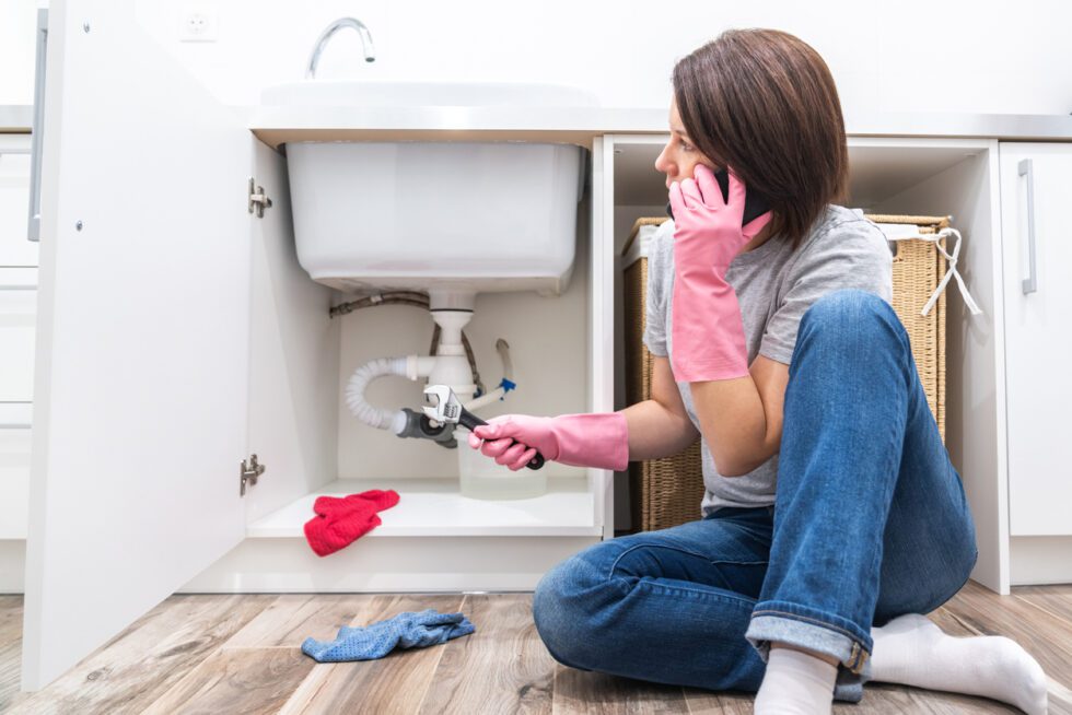 Avoiding costly plumbing mistakes - Woman calling a plumber to fix a plumbing issue at home.