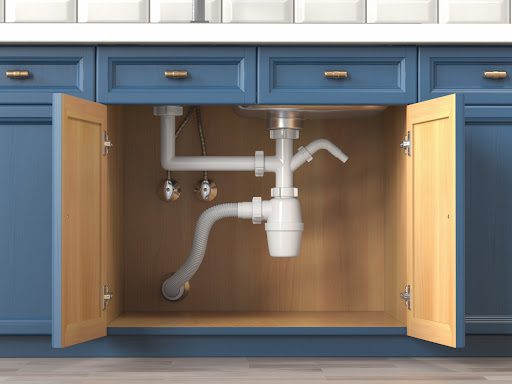 A kitchen cabinet with its doors open showing the pipes and siphon of a kitchen sink.